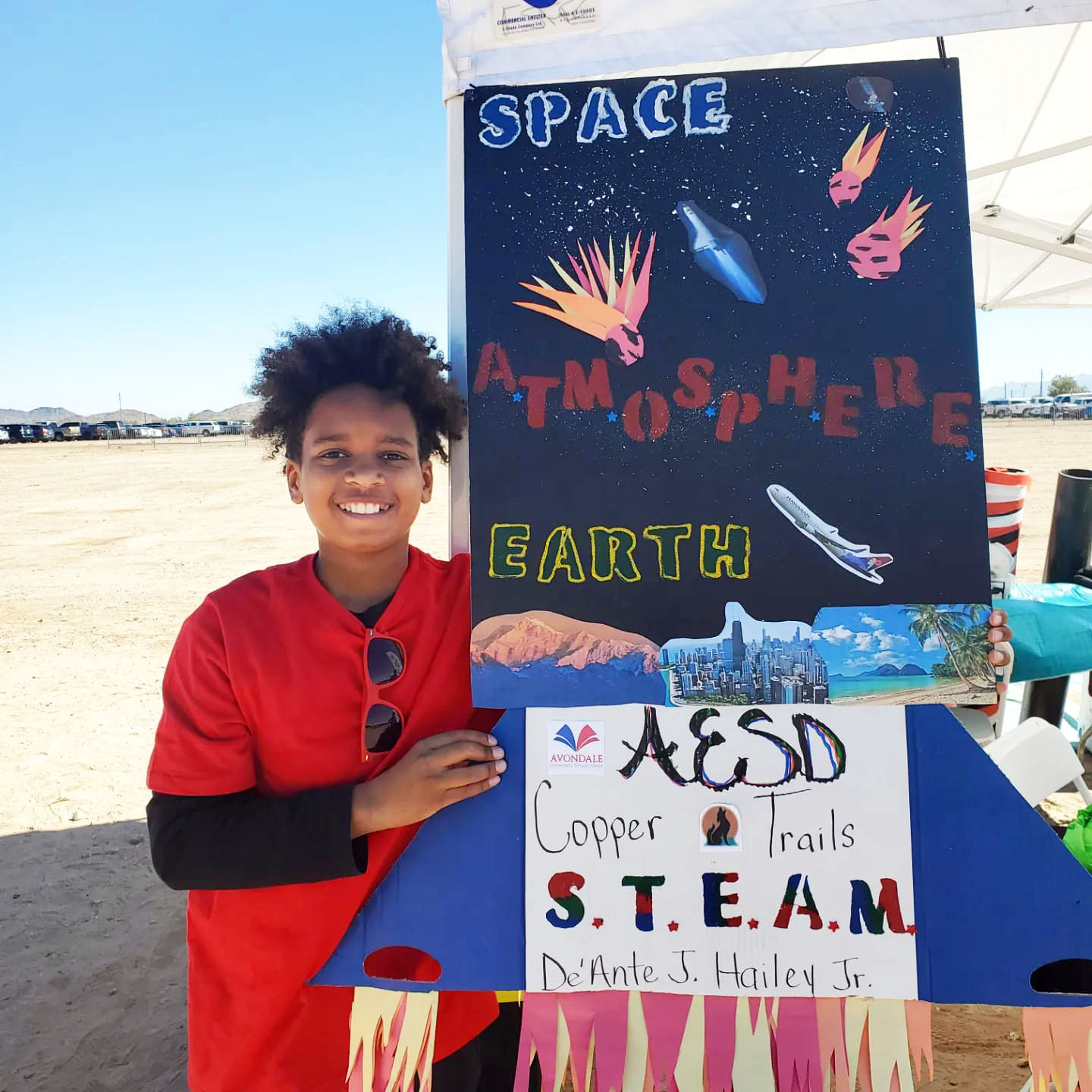 Un niño sonriente sostiene un panel colorido para un proyecto de ciencias