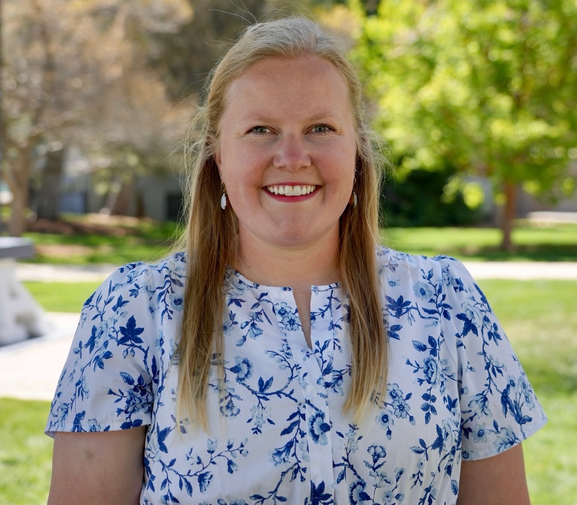 Smiling woman in a blue and white floral blouse standing outdoors on a sunny day.