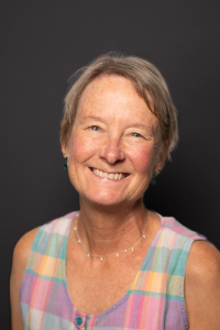 A smiling woman with hair wearing a plaid sleeveless top.
